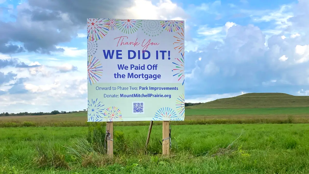 Mortgage payoff sign in park Park sign reading Thank you — We did it, we paid off the mortgage, with hill and grassy field in the distance