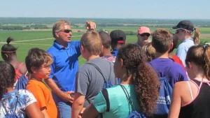 Man teaching a group of children while they view the farm country in the distance