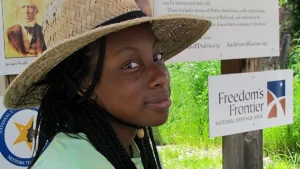 Young Black woman in a straw hat smiling gently at the camera inside the kiosk sun-shade learning area