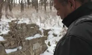 Close-up of a Black man looking down with a snow-covered rock formation in the background